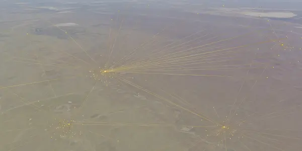 An aerial view of a barren landscape with radiating yellow lines connecting clusters of bright dots, set against a muted, hazy backdrop.