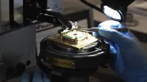 A technician carefully handles a complex electronic component on a specialized workstation in a darkened laboratory.
