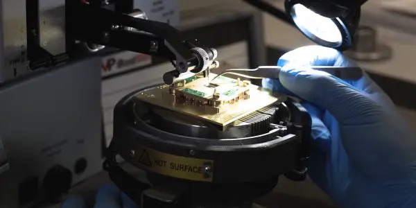 A technician carefully handles a complex electronic component on a specialized workstation in a darkened laboratory.