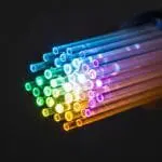 Optical fiber strands glowing in rainbow colors spreading out from the end of a dark cable.
