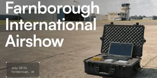 A black flight case containing electronic equipment sits on a tarmac with a control tower in the background, showcasing dark grey and black tones.