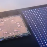A complex circuit board and a grid of illuminated points are displayed in a dark laboratory setting, with blue and pink hues.