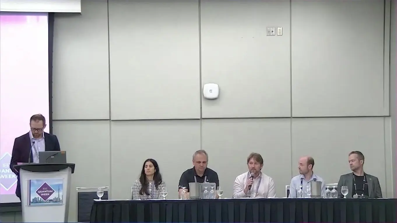 Quantum Hpc Integration At Qce26 Became A Question Of Shared Words Moderator at the lectern and five panellists at a table on quantum HPC integration in 2026
