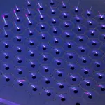 A hexagonal array of purple laser beams shine upwards from a dark metallic surface, creating a futuristic, high-tech aesthetic.