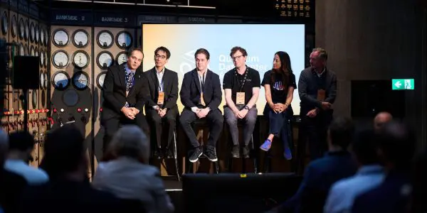 A panel discussion takes place on a stage with a backdrop of electrical diagrams, in shades of grey and black.
