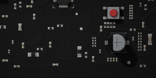 A dark grey circuit board with silver and black components is lit from above, creating strong highlights and shadows.