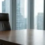 An empty office chair at a boardroom table against a glass tower wall