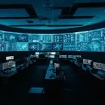 A darkened operations room facing a curved wall of monitoring displays