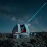 Telescope dome on a rocky summit firing a cyan laser beam into a starry night sky