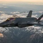 Illustration of a stealth fighter jet with US markings flying above snow-capped mountains and clouds at sunset
