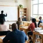 Adult learners at desks facing a whiteboard of faint diagrams