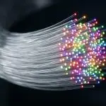 A swirling bundle of optical fibres glows with vibrant, multicoloured light against a dark, blurred background.