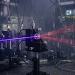 Violet laser beam striking a crystal on an optical mount and splitting into two red cones