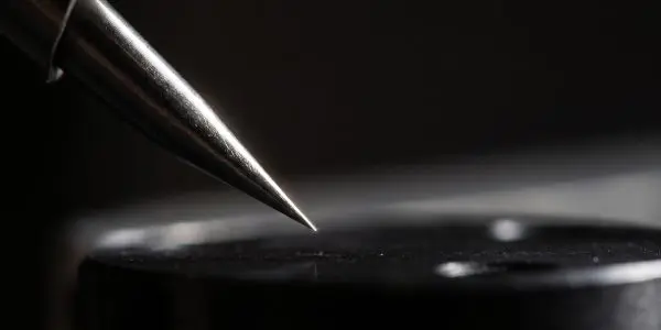 Sharp metal probe tip poised just above a dark sample surface