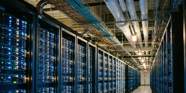 a long data centre aisle lined with server racks under overhead cable trays and pipes
