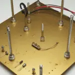 A brass plate with metal posts and wiring is lit from above, creating a complex, golden and silver arrangement.