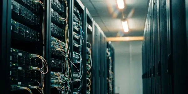 A server room aisle with open racks of cabled equipment on the left and closed cabinets on the right