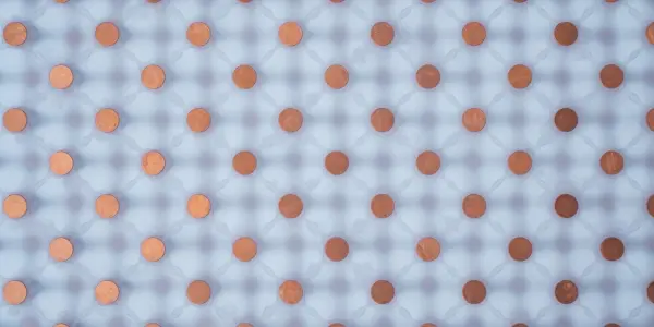 A grid of pennies covers a translucent plastic sheet, creating a patterned shadow against a black background, using copper and white.