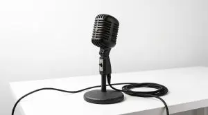A vintage black microphone stands on a white table against a stark white background, creating a minimalist composition.