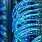 Glowing blue fibre optic patch cables plugged into a server switch with blurred racks behind