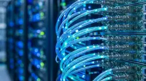 Glowing blue fibre optic patch cables plugged into a server switch with blurred racks behind