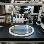 A silicon wafer on a bench beside a microscope