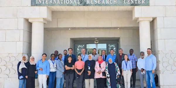 A group of people stands outdoors in front of the Sesame International Research Center building.