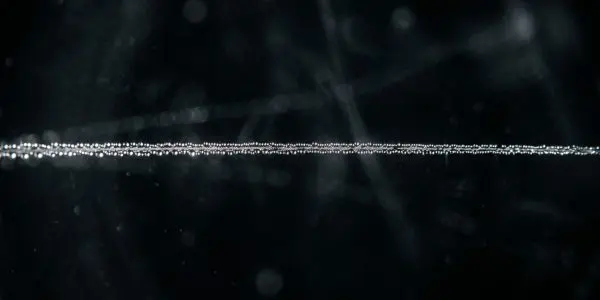A straight trail of fine droplets across a dark field