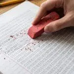 A hand erasing pencilled binary digits from a notepad