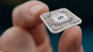 A small, silver electronic device is held delicately in a human hand against a dark blue background.