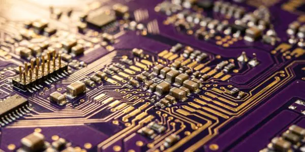 A close-up of a purple circuit board with gold traces and tiny electronic components, illuminated with warm light.
