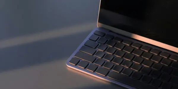 An open laptop sits on a dark surface, illuminated by warm light, with a screen displaying a dark, starry background.