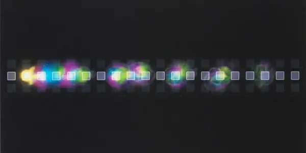 A dark laboratory setting displays a linear array of glowing, colourful squares, transitioning from yellow to purple.