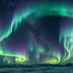 Green aurora curtains over a frozen coast