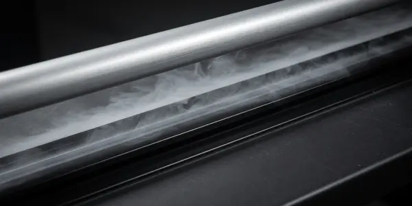 A close-up of a metallic surface with wisps of white vapour rising from it, set against a dark background.