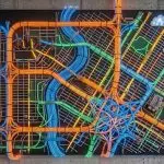 A large, illuminated map of roadways dominates a modern office space with city views, using vibrant blues, oranges, and greens