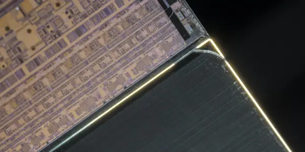 A microchip die, intricately patterned in gold and silver, is dramatically lit against a black background, suggesting advanced technology.
