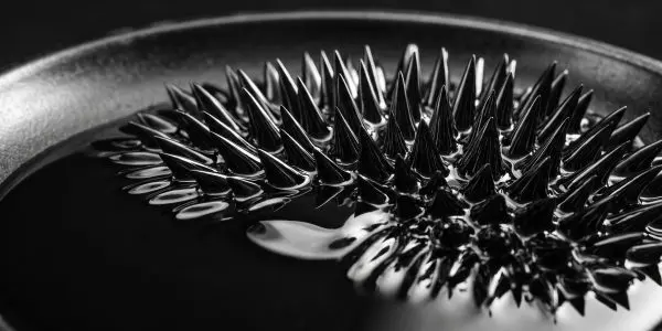 Black ferrofluid rising into sharp spikes in a shallow dish, shot in monochrome