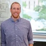 Man in button-down shirt next to whiteboard with physics equations