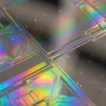 A close-up of a microchip's patterned surface displays iridescent colours, set against a dark background, creating a futuristic aesthetic.