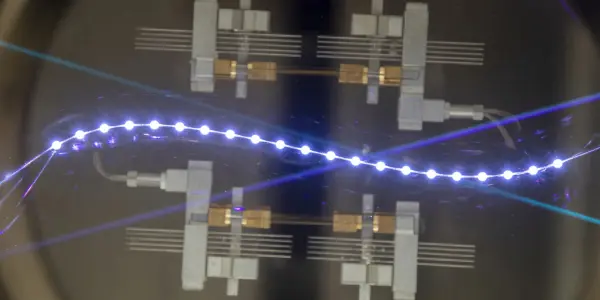 A dark laboratory setting features a complex array of metallic structures connected by a glowing, blue, bead-like chain.