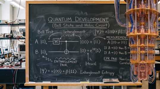 A chalkboard displays quantum development concepts alongside a complex, multi-coloured quantum computing apparatus.