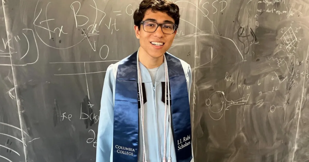 Luca Nashabeh wearing Columbia University regalia in front of a blackboard with physics equations before his Columbia