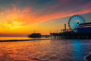 The vibrant sunset casts a warm orange and pink glow across the ocean, reflecting on the calm water and sky.