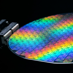 An iridescent silicon wafer held by a robotic arm