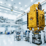 Technicians in white coveralls working around a gold-foil-wrapped satellite in a cleanroom