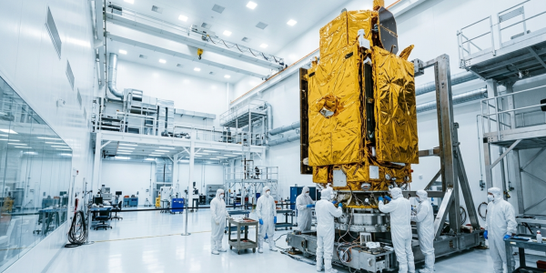 Technicians in white coveralls working around a gold-foil-wrapped satellite in a cleanroom
