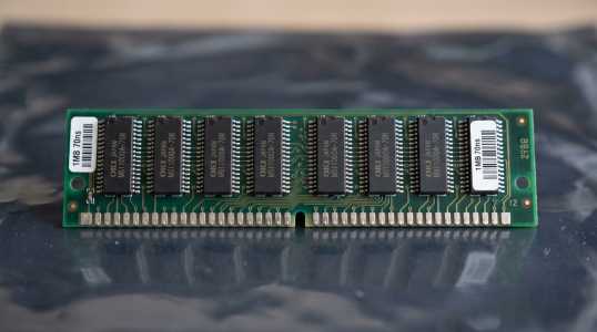 A close-up shot shows a single stick of RAM memory against a dark purple background, with green accents.
