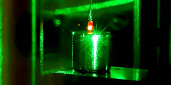 Photograph with a small square diamond glowing red as a result of being illuminated with a green laser, suspended above