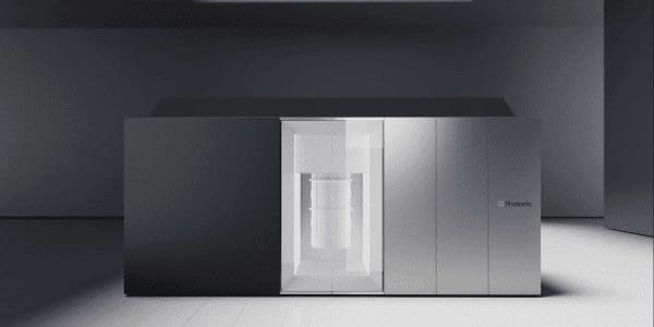 A sleek, modern 3D printer stands on a polished floor in a minimalist, dark room with grey walls.